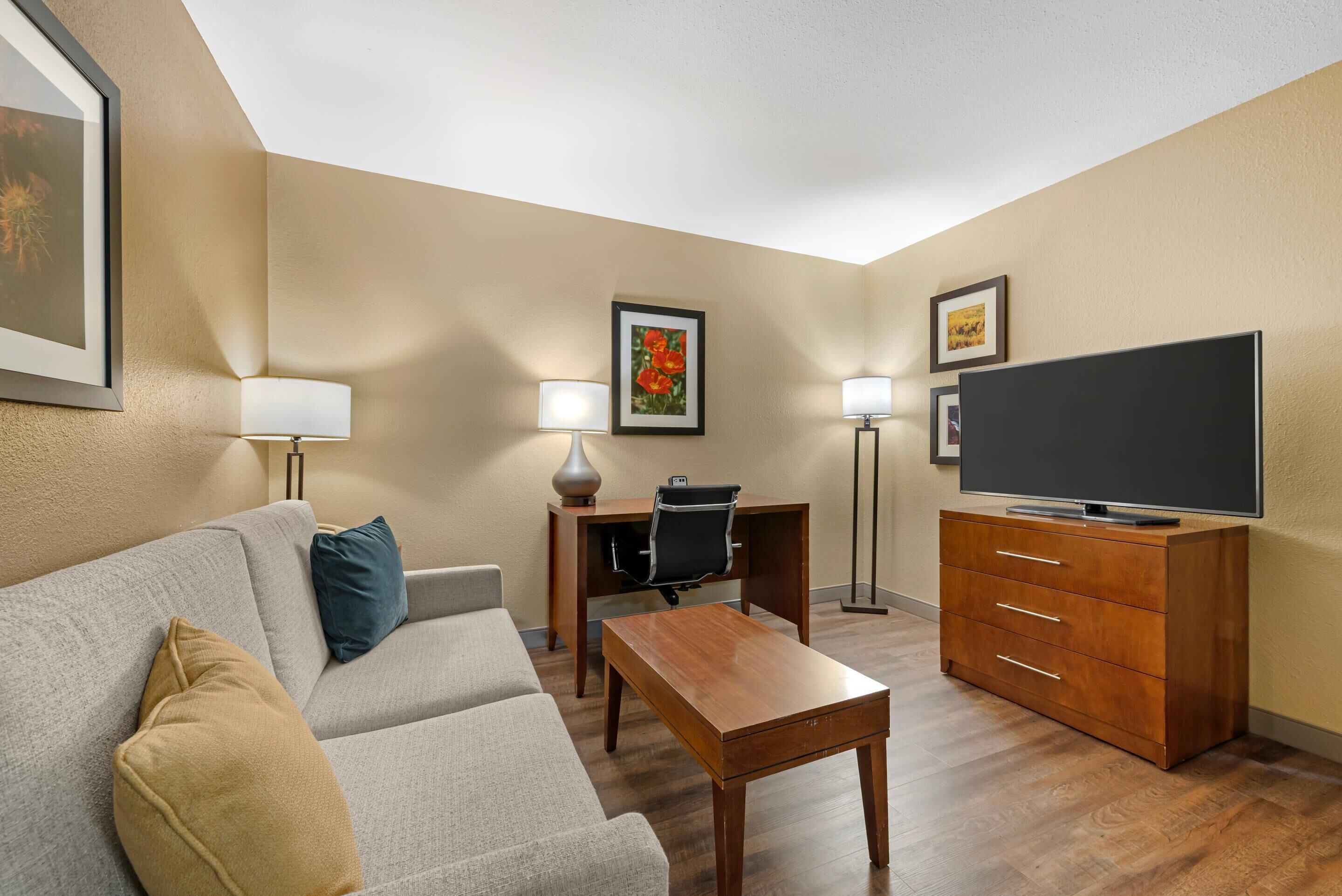 Ein modernes Hotelzimmer mit einer Couch, einem Holztisch, einem Fernseher und zwei Wandlampen.