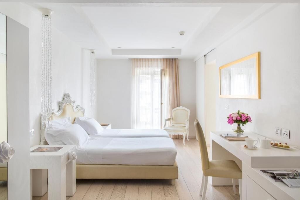 A hotel room with two beds, a desk, a chair, a mirror, and a window with curtains.