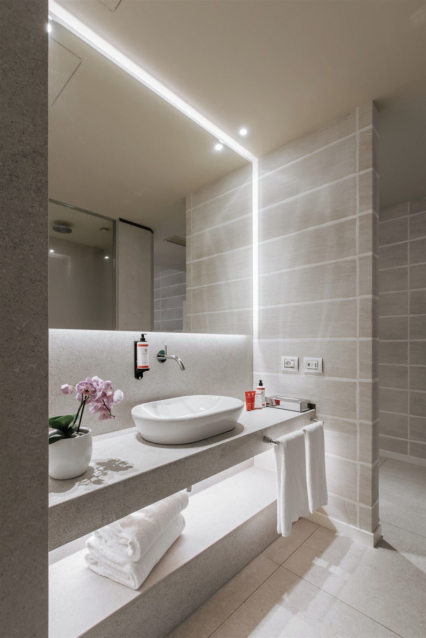A modern bathroom with a large mirror, white sink, and a shower area.