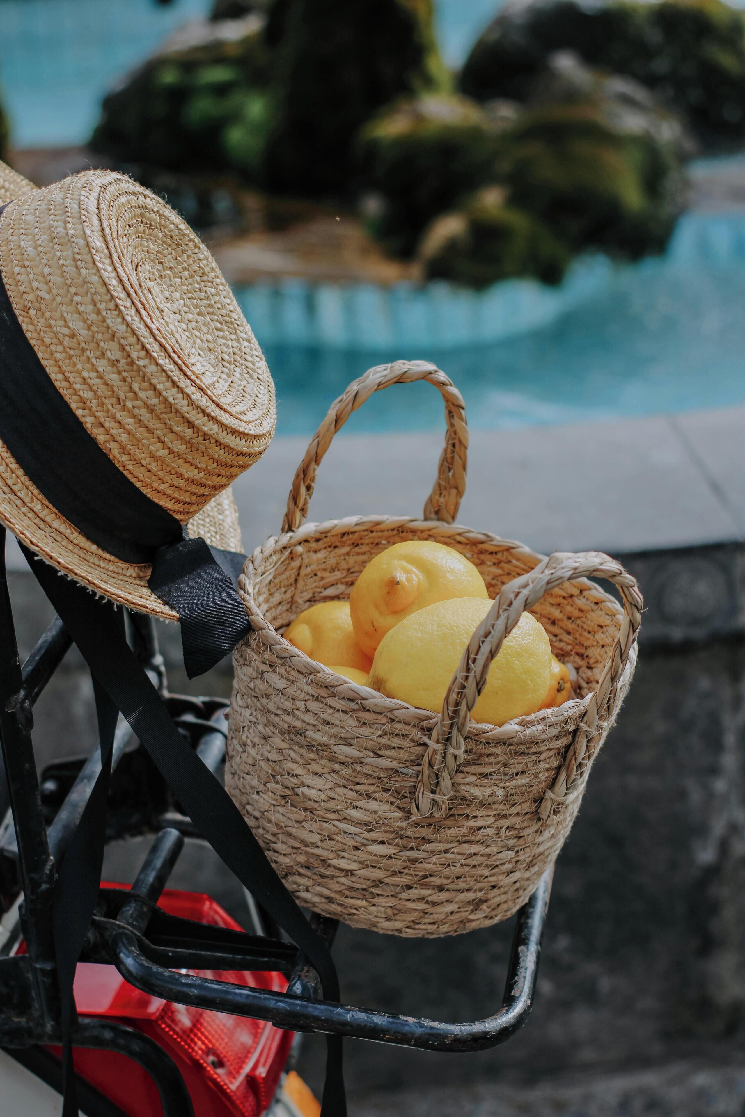 Un panier en osier contenant des citrons, posé sur une chaise près d’une piscine.