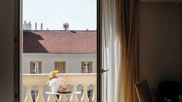 A balcony with a table and chairs, a view of buildings, and a door with curtains.