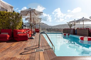 A wooden deck with red lounge chairs and umbrellas overlooking a pool.