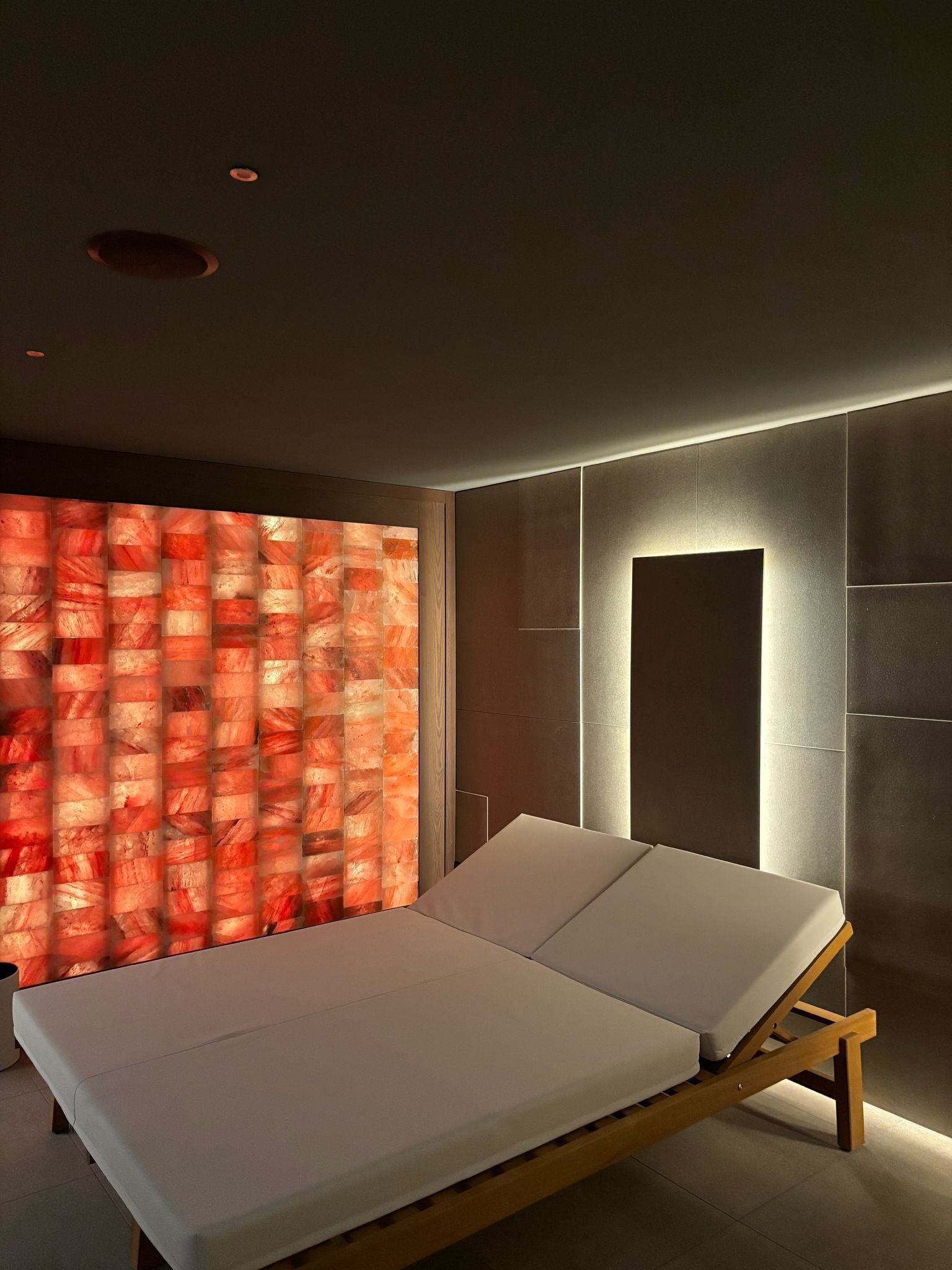 A modern room with a bed, a wall with a textured pattern, and a recessed ceiling light.