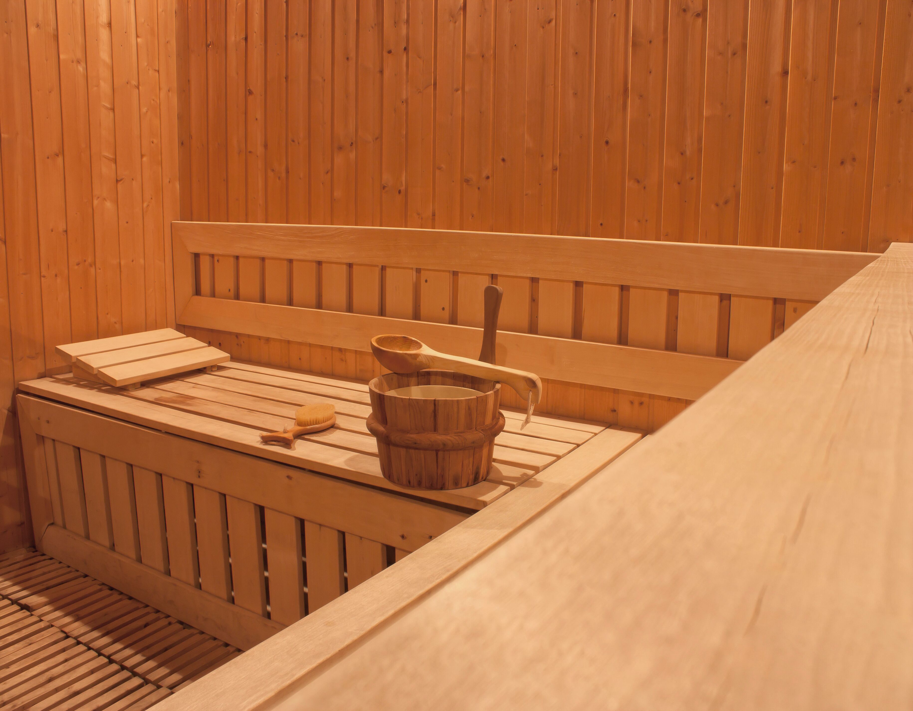 Un sauna en bois avec des bancs, un seau en bois et une brosse en bois.