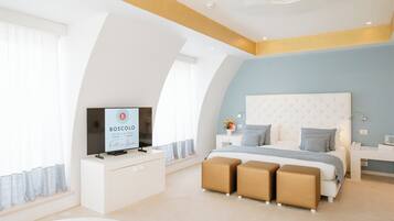 A modern bedroom with a large bed, a TV on a white console, and a ceiling fan.