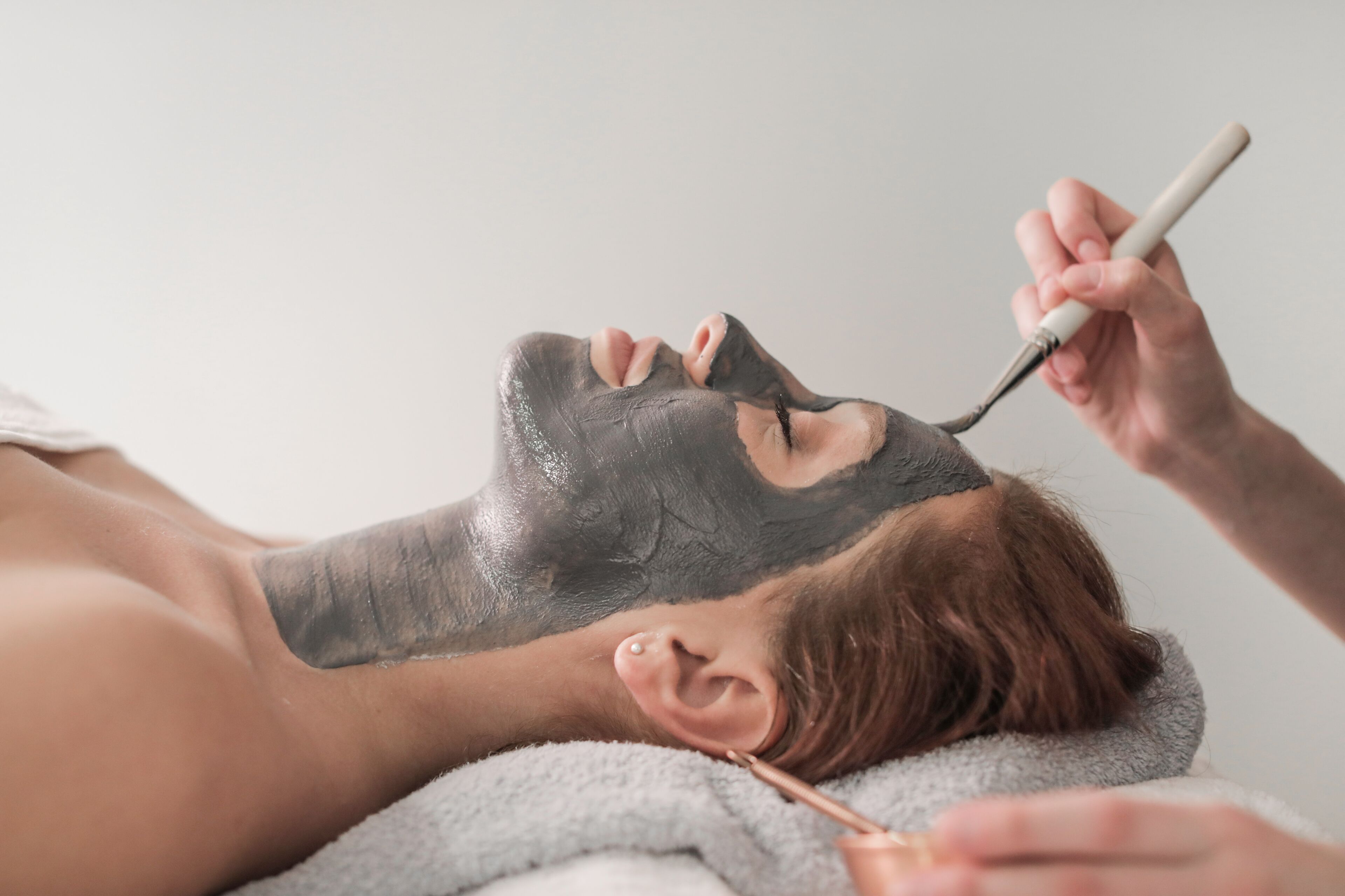Una persona recibiendo un tratamiento facial con una mascarilla negra.