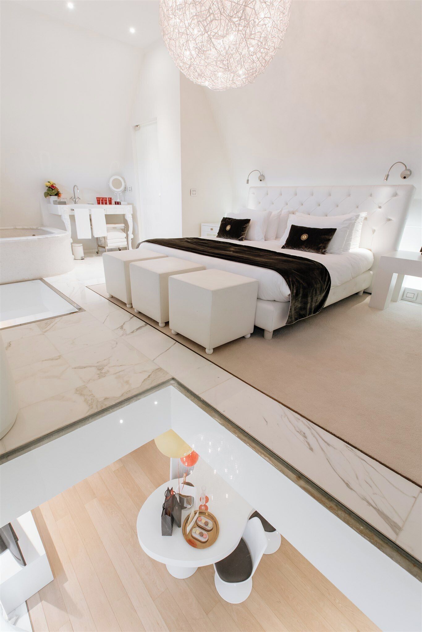 A modern bedroom with a large bed, bedside tables, a vanity, and a glass coffee table.