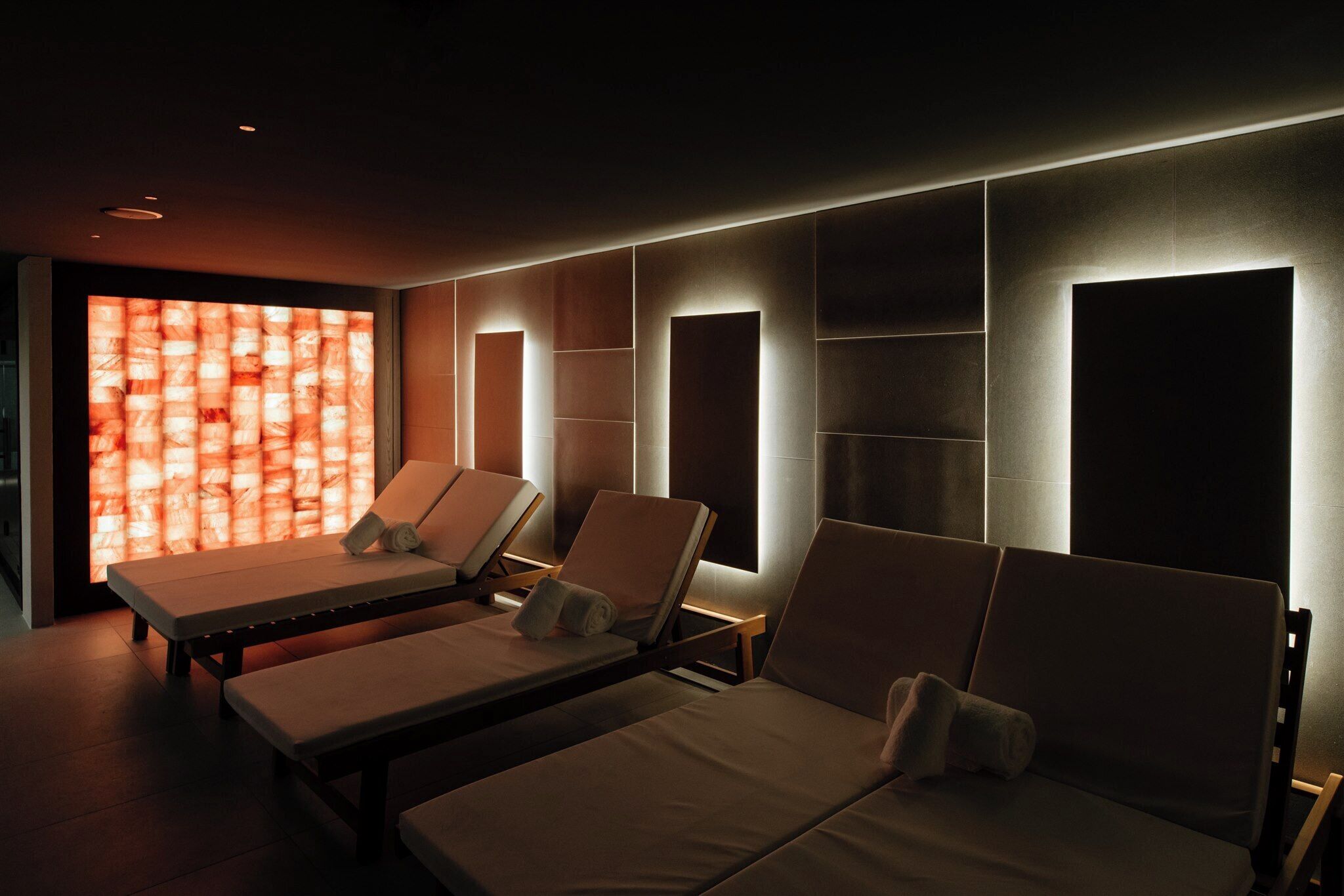 Une salle de spa équipée de trois tables de massage, d’un mur à motifs en relief et d’un éclairage encastré.