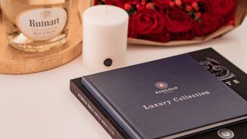 A bottle of Ruinart champagne, a white candle, a bouquet of red roses, and a book titled 'BOSCOLO Luxury Collection'.