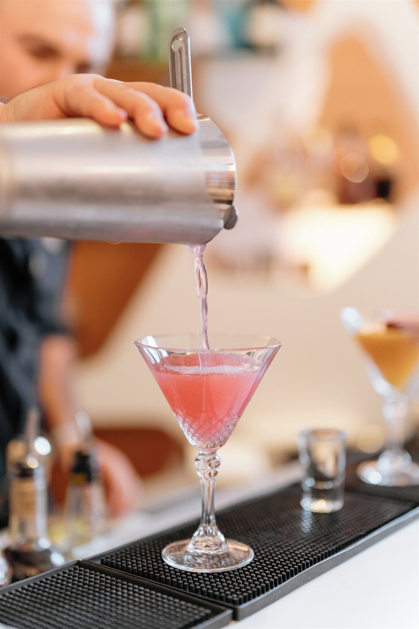 A bartender pouring a pink drink into a martini glass.