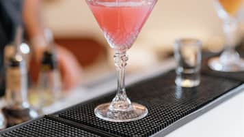 A bartender pouring a pink drink into a martini glass.