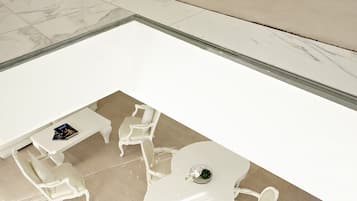 Une chambre d’hôtel moderne avec une table et des chaises blanches, un petit banc blanc et une cloison en verre.