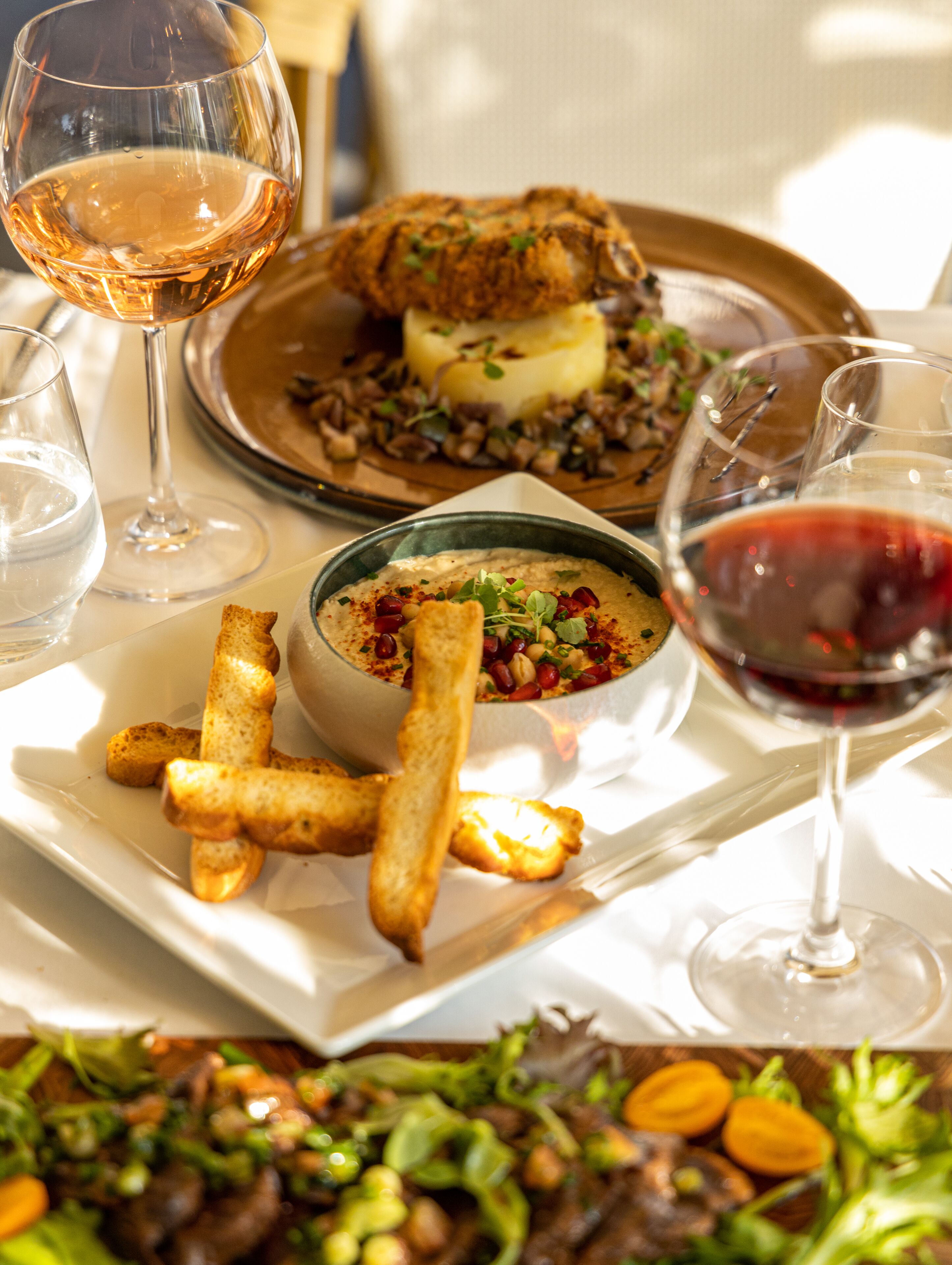 Une table à manger avec un poulet rôti, un bol de sauce, des frites et des verres à vin.