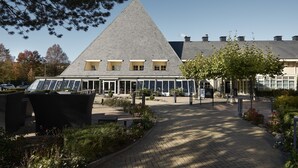 A modern building with a triangular roof, large windows, and a paved walkway with greenery.