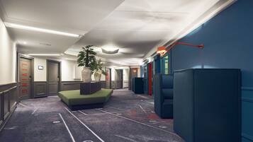 A hotel corridor with a green seating area, a potted plant, and a blue wall with a basketball hoop.