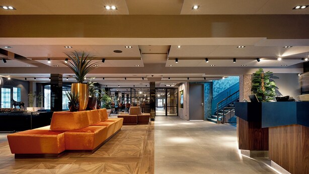 A spacious lobby with a modern design, featuring a reception desk, seating area, and a staircase.