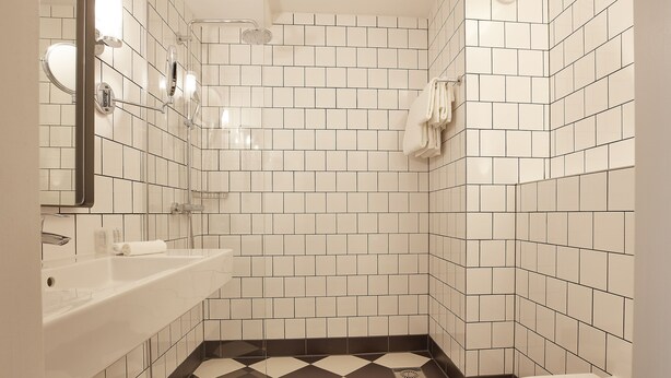 A bathroom with white and black checkered floor tiles, a white sink, and a toilet. - Carlton President (Utrecht)