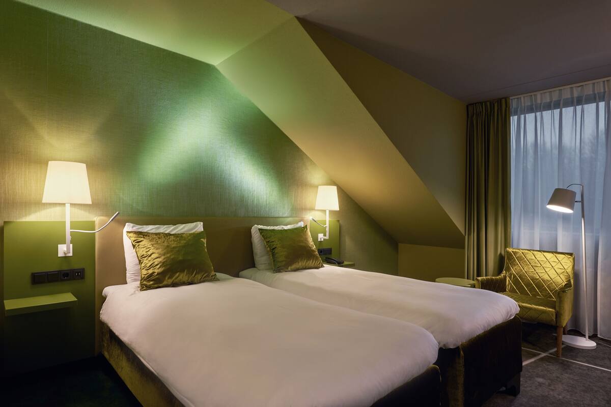 A hotel room with two beds, green walls, and a modern design.