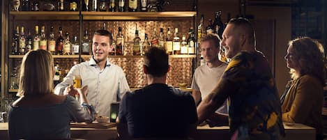 A bar area with a bartender and patrons. There are shelves with various bottles and glasses.