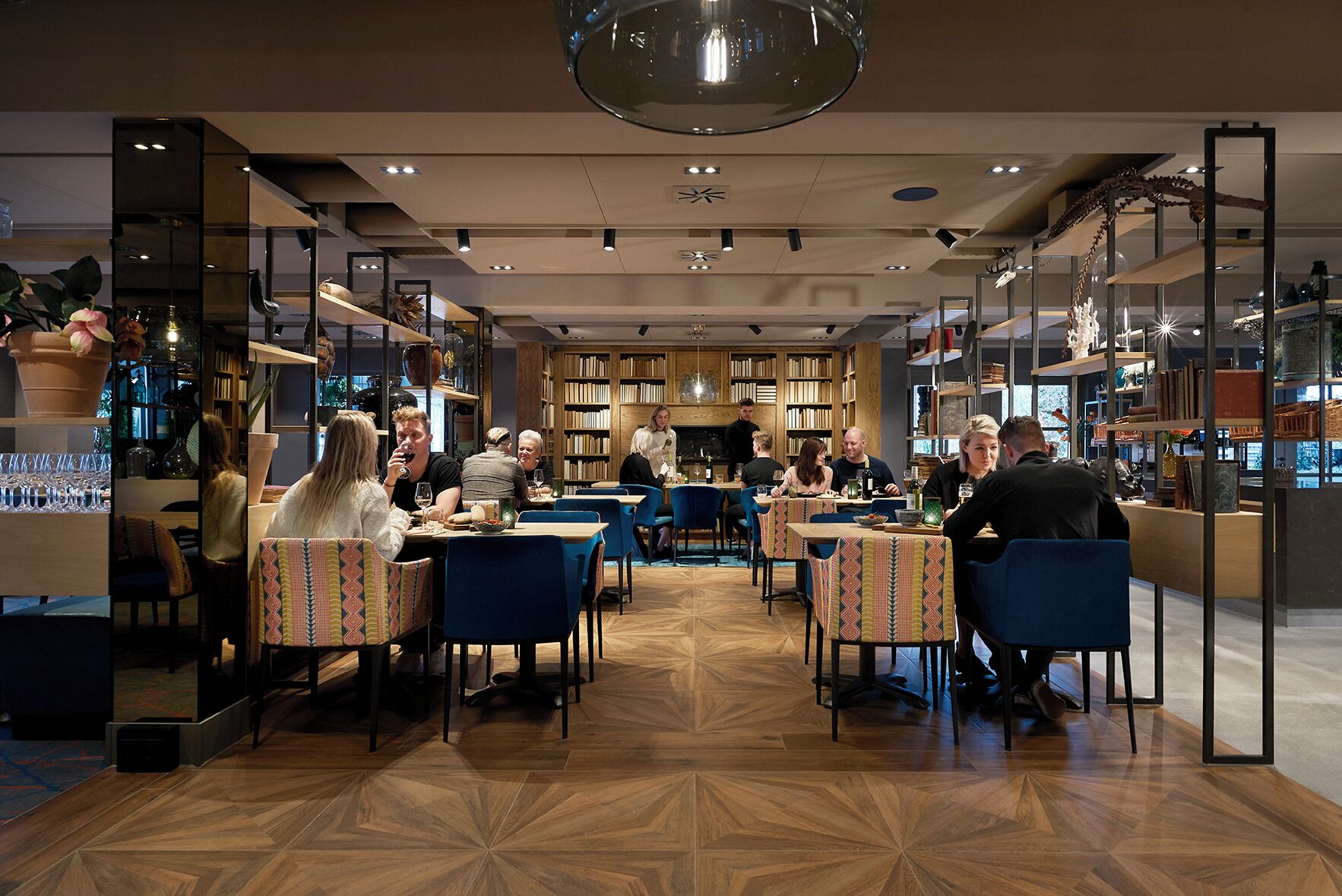A modern restaurant with wooden floors, blue chairs, and tables with patterned tablecloths.