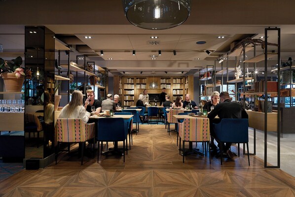 A modern restaurant with wooden floors, blue chairs, and tables with patterned tablecloths.