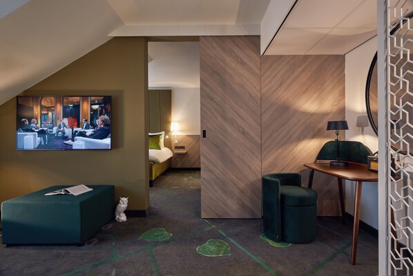 A modern hotel room with a large TV, a sofa, a desk, and a bed.