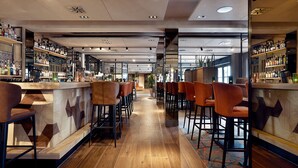 A bar area with wooden flooring, bar stools, and shelves of bottles.