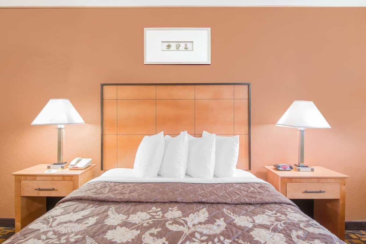 A hotel room with a large bed, two bedside tables with lamps, a framed picture on the wall, and a wooden headboard.