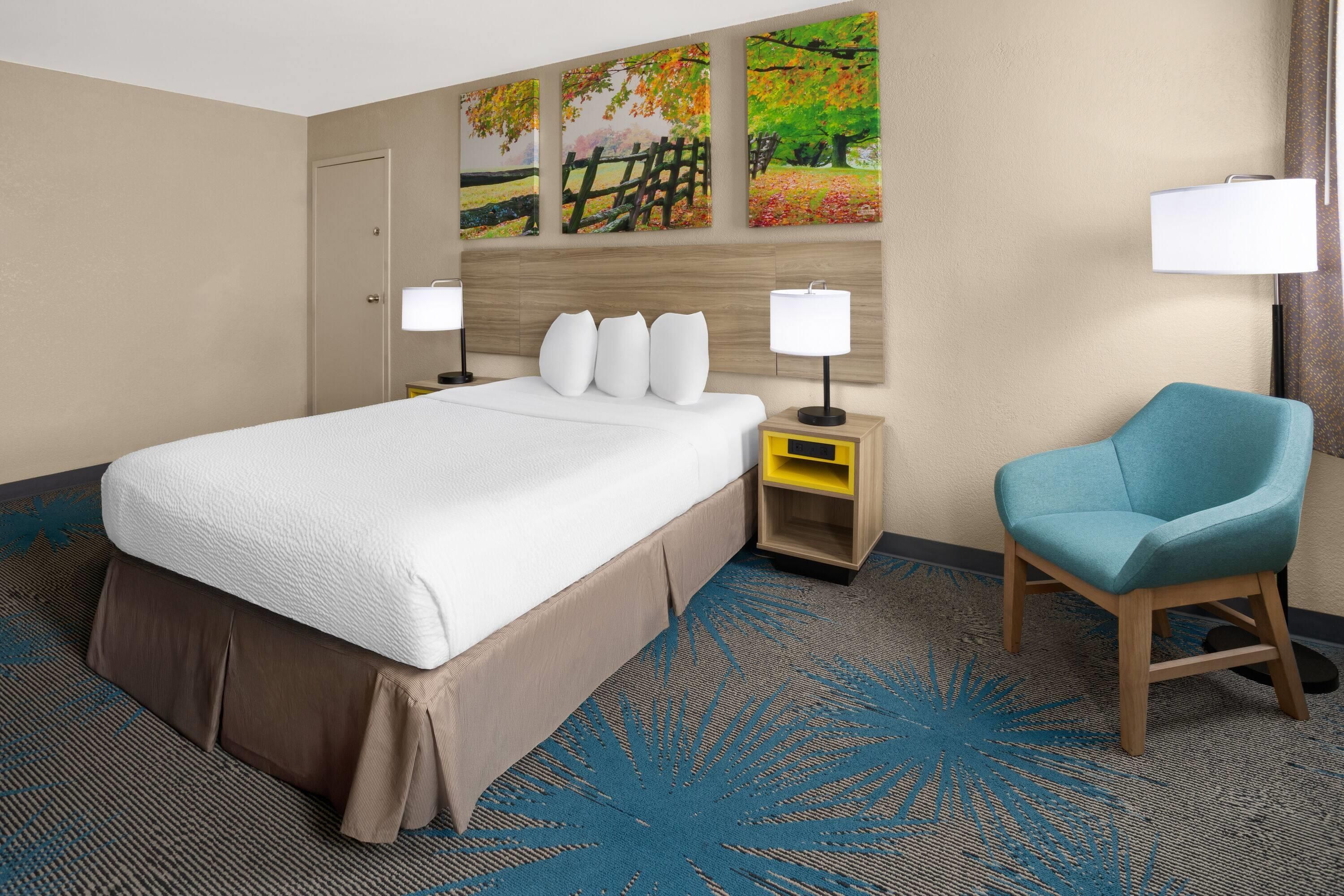 Ein Hotelzimmer mit einem großen Bett, einem Sessel, einem Nachttisch und einer Wand mit drei Bildern.