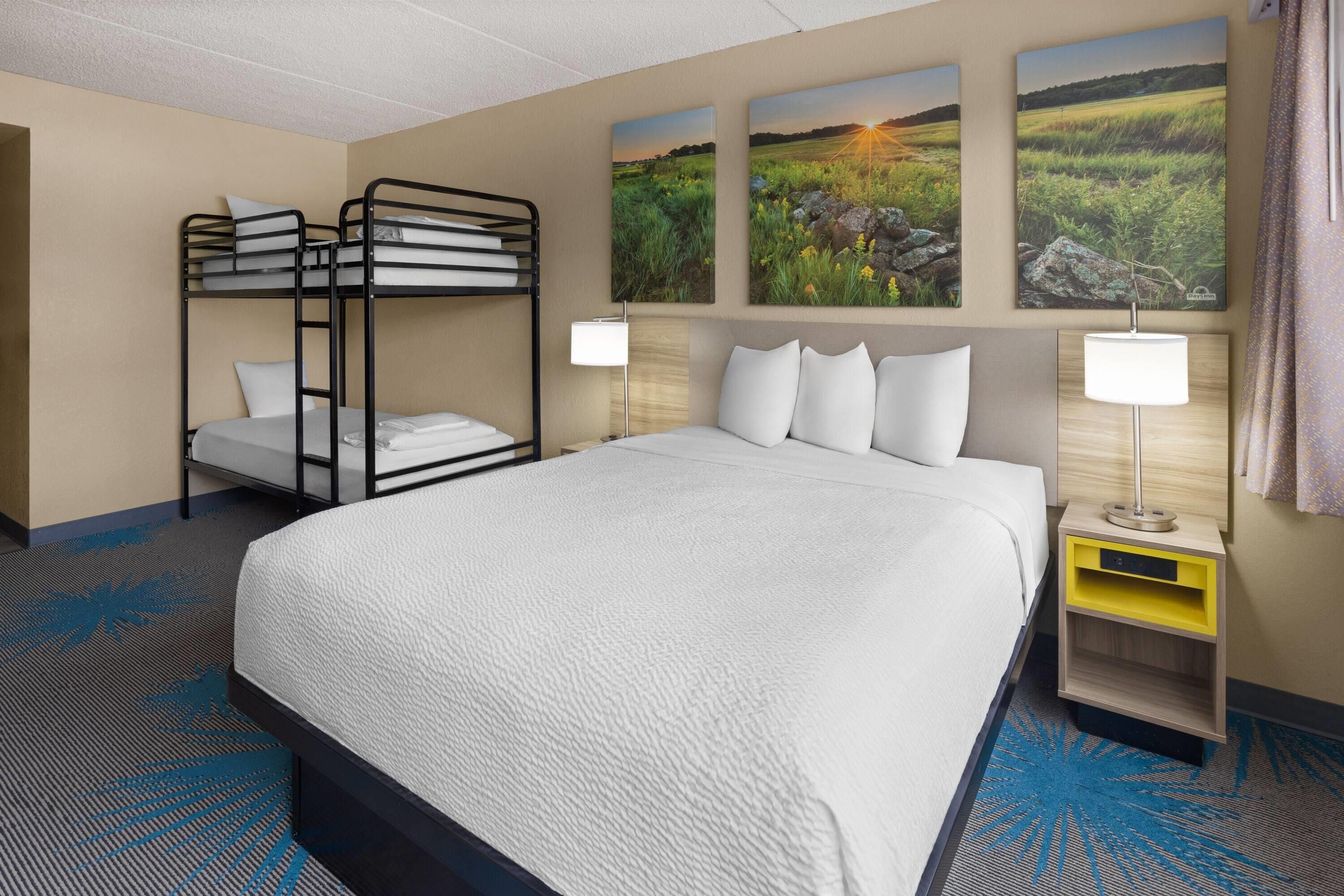 A hotel room with a bunk bed, a single bed, a nightstand with a lamp, and three landscape paintings on the wall.