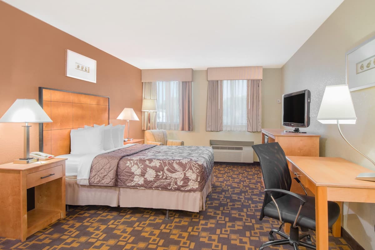 A hotel room with a bed, desk, chair, TV, and two lamps.