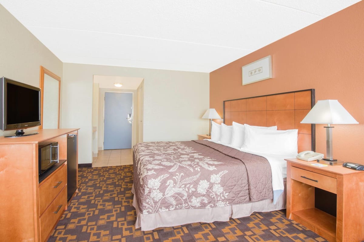 A hotel room with a bed, bedside lamps, a television on a dresser, and a patterned carpet.