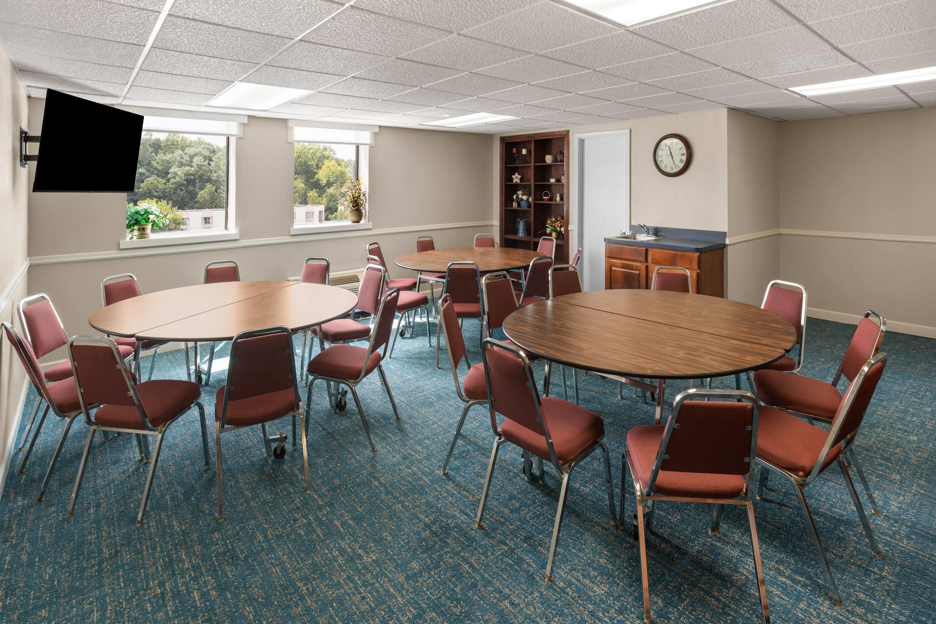 A conference room with round tables and chairs, a bookshelf, a clock, and a TV mounted on the wall.