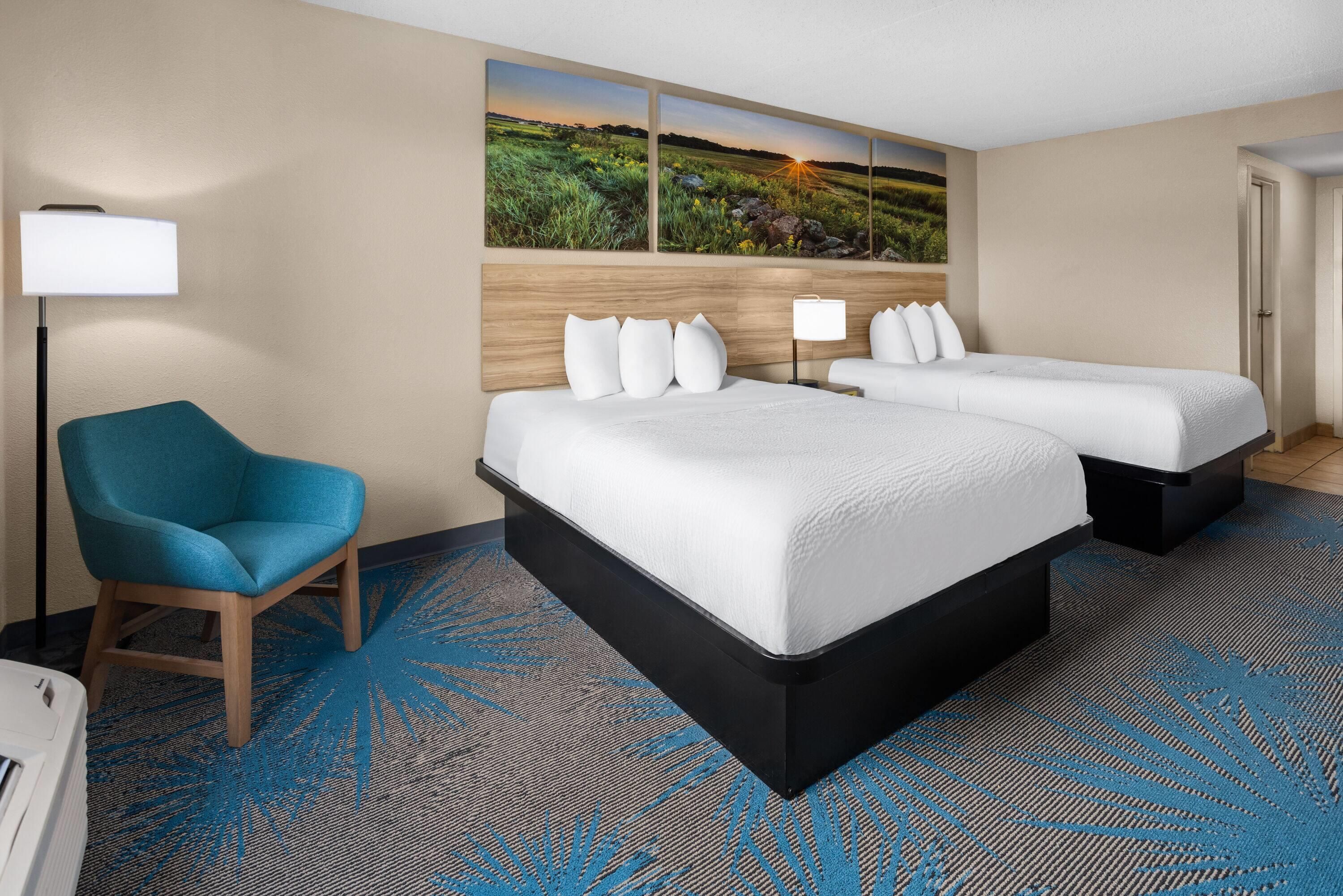 A hotel room with a large bed, a chair, a desk, and a painting of a landscape.