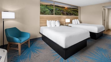 A hotel room with a large bed, a chair, a desk, and a painting of a landscape.