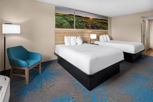 Habitación de hotel con una cama grande, una silla, un escritorio y un cuadro de un paisaje.