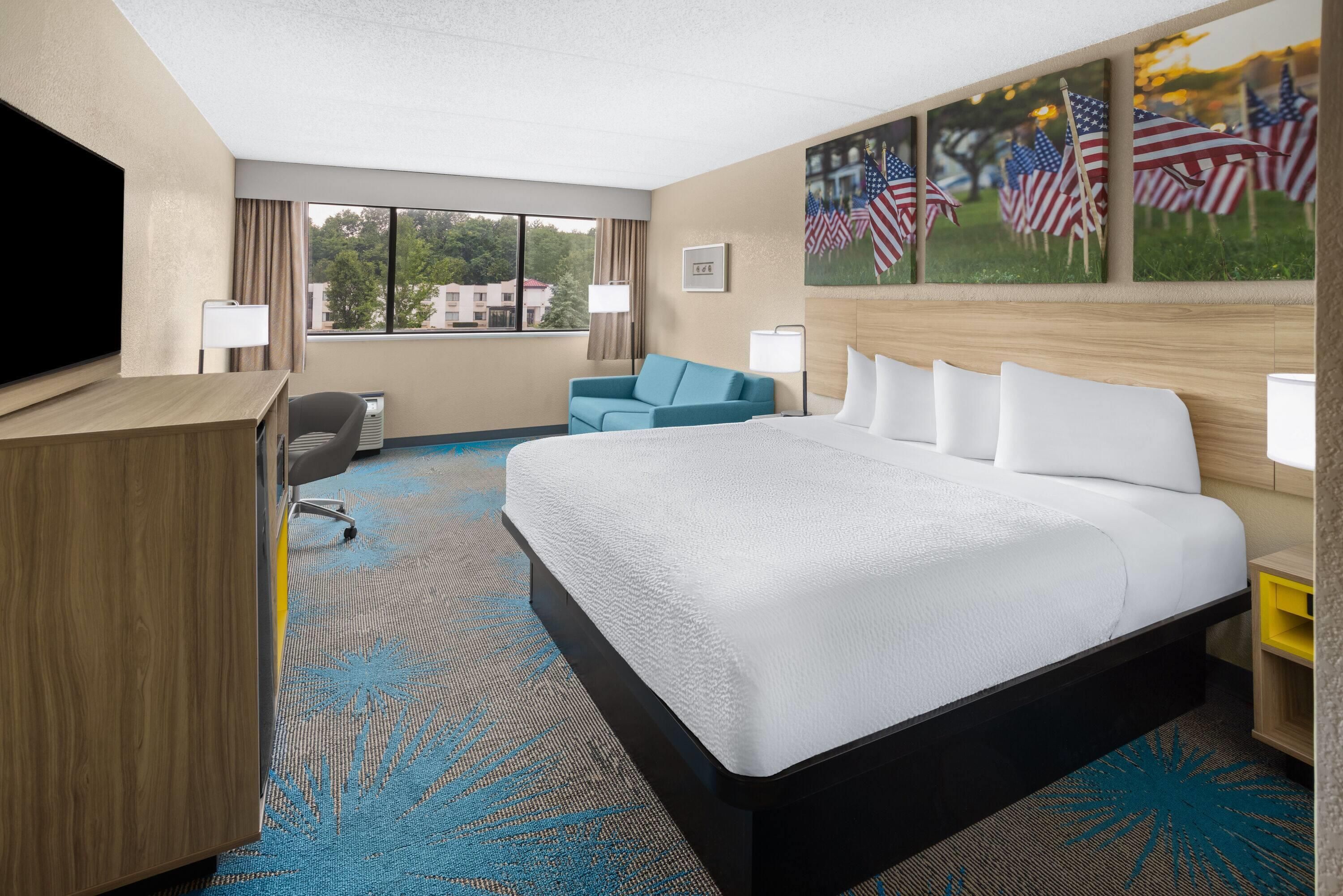 A hotel room with a large bed, a desk, a chair, and a view of the outdoors.