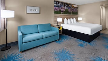Une chambre d’hôtel avec un lit, un canapé bleu, une table de chevet, une lampe et un tableau au mur.