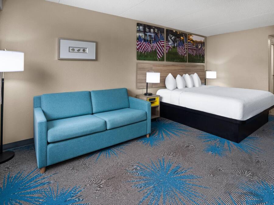 Une chambre d’hôtel avec un lit, un canapé bleu, une table de chevet, une lampe et un tableau au mur.
