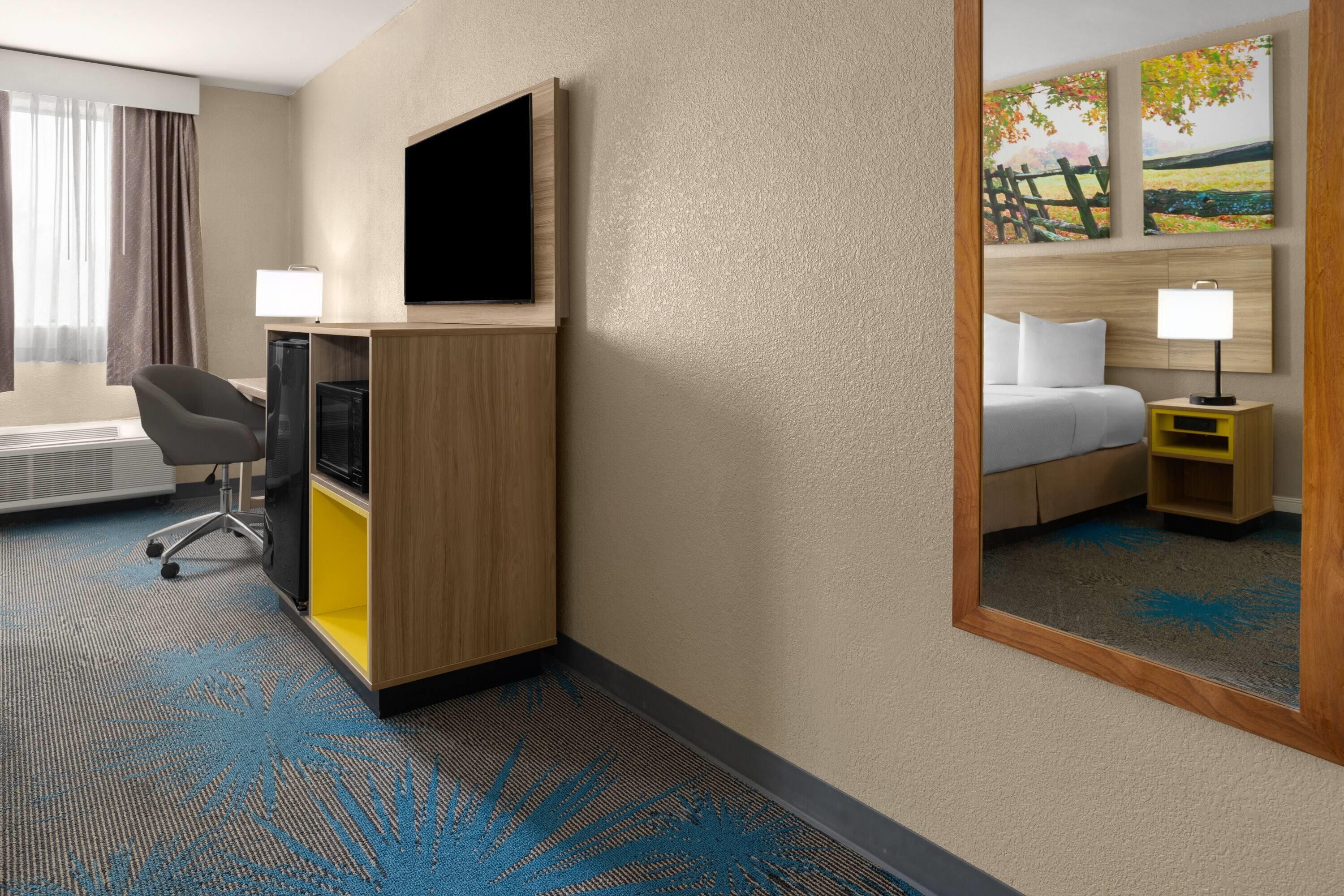 A hotel room with a bed, a desk with a computer, a chair, a TV, and a painting on the wall.