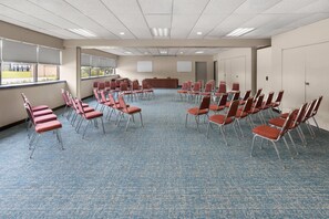 Une salle de conférence avec des rangées de chaises, un pupitre et un tableau blanc.
