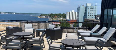 A rooftop terrace with outdoor seating, a view of the water, and city buildings in the background.