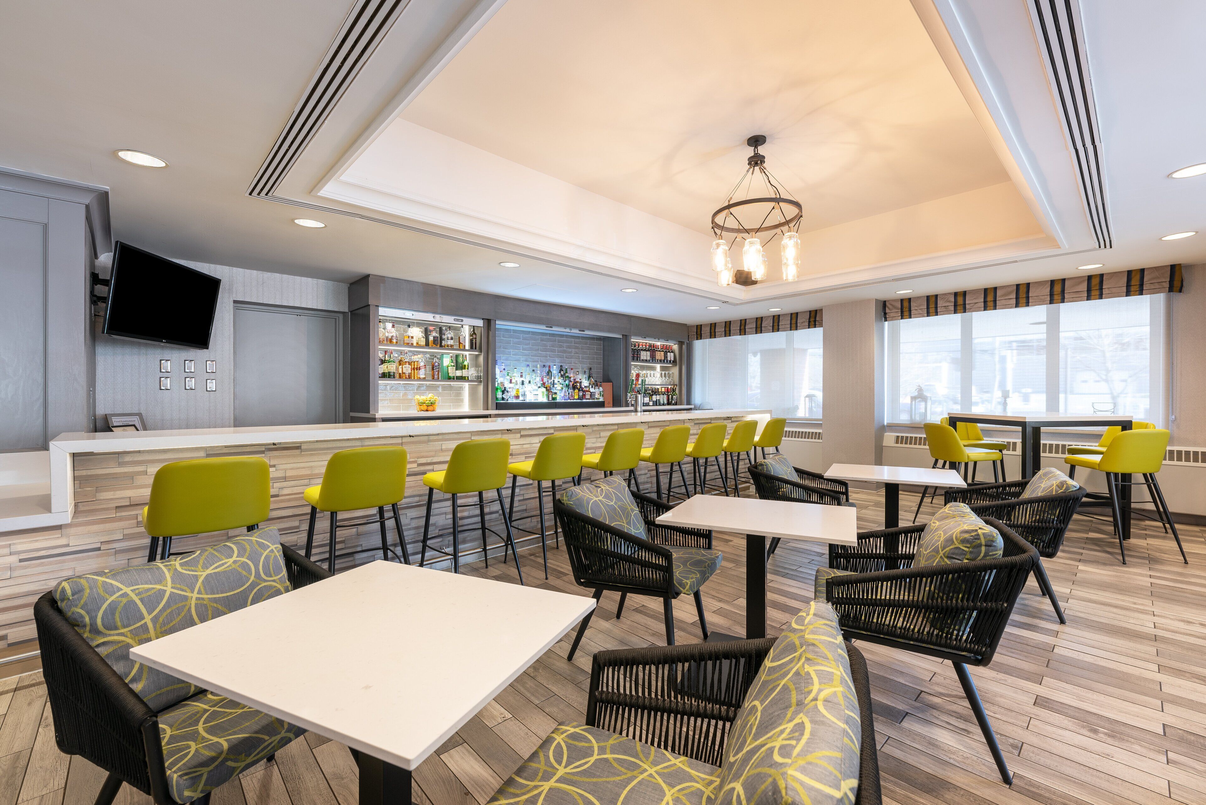 En moderne restaurant med barområde, gule stole og forskellige siddepladser, herunder borde og sofaer.