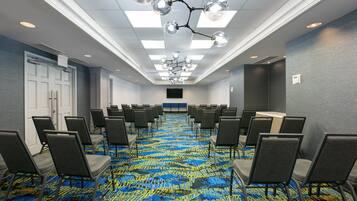 A conference room with rows of chairs, a patterned carpet, and a modern chandelier.