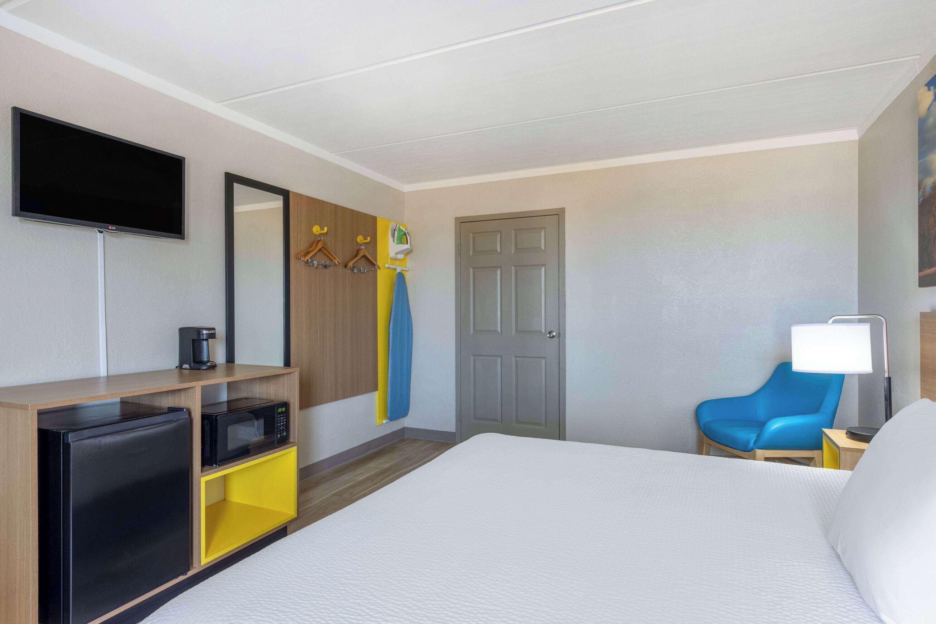 A hotel room with a bed, a desk with a microwave, a television, a door, and a chair.