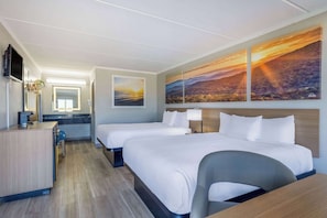 A hotel room with two beds, a desk, a chair, a TV, and artwork on the wall.