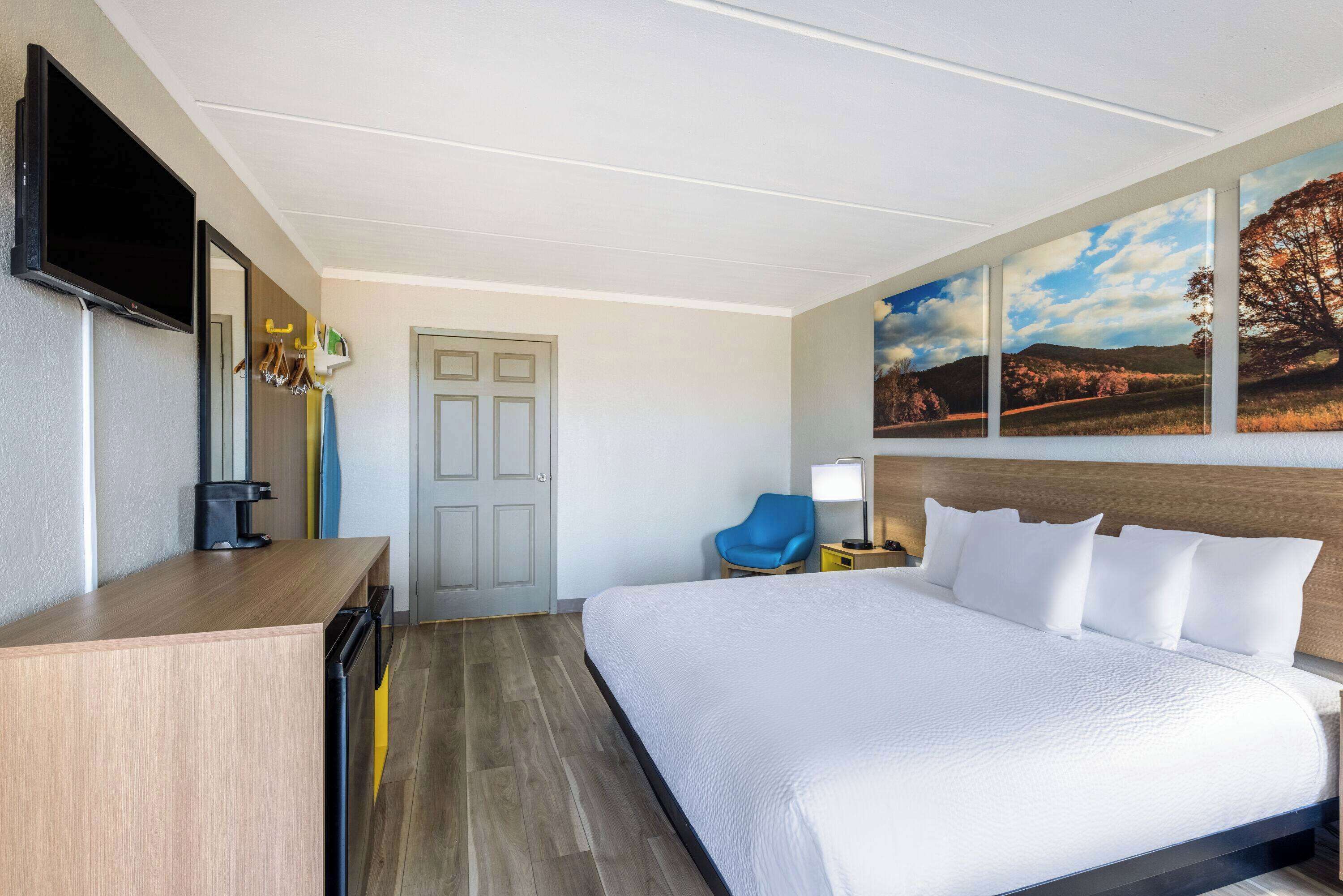 A hotel room with a bed, a desk, a chair, a TV, and artwork on the wall.