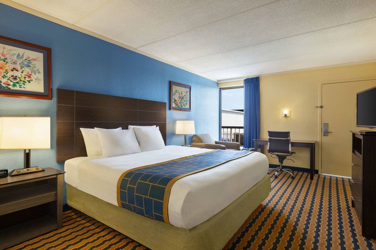 Une chambre d’hôtel avec un grand lit, un bureau, une chaise, une télévision et une fenêtre avec des rideaux.