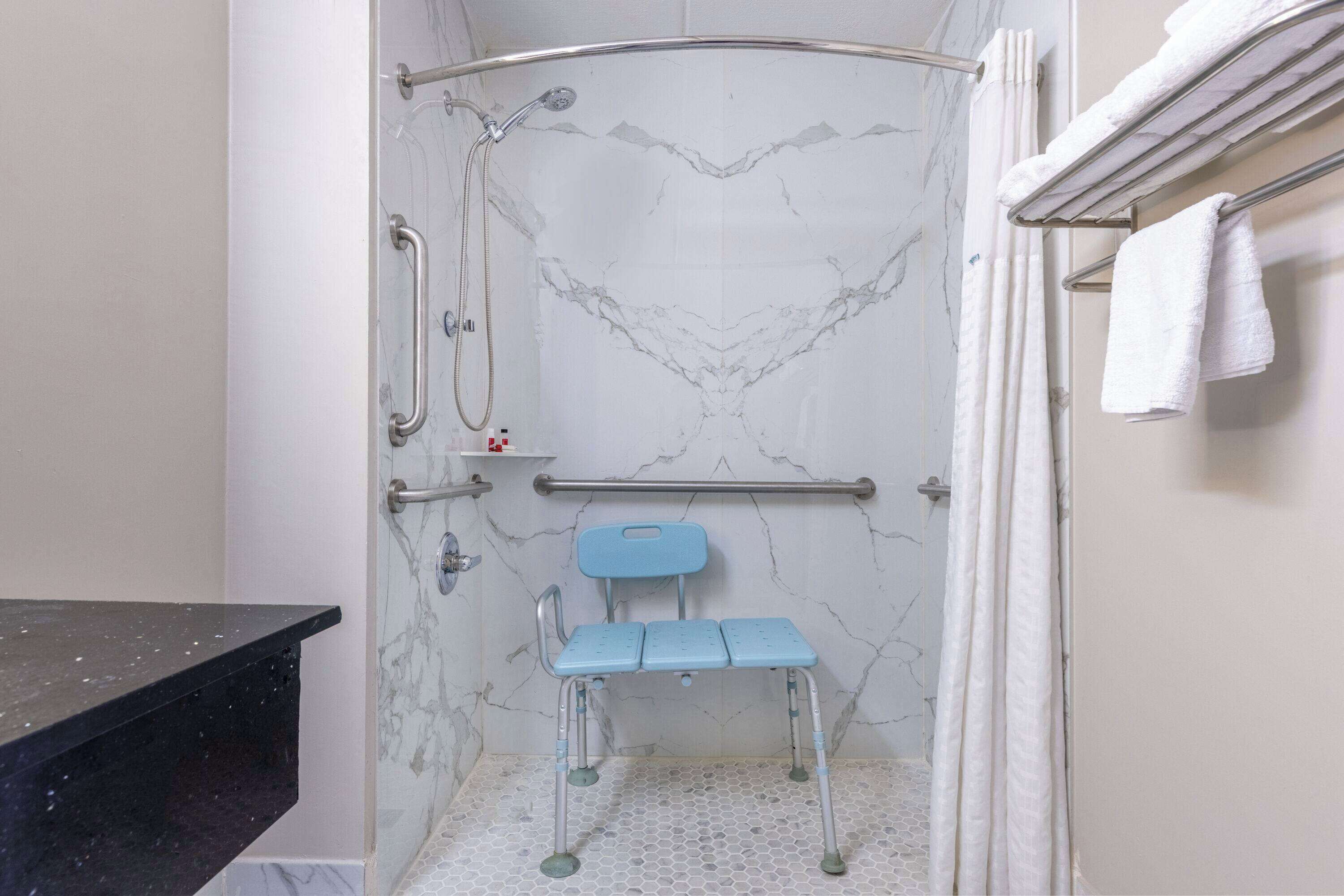 Een badkamer met een douche, een handgreep, een rolstoeltoegankelijke bank en een handdoekhouder.