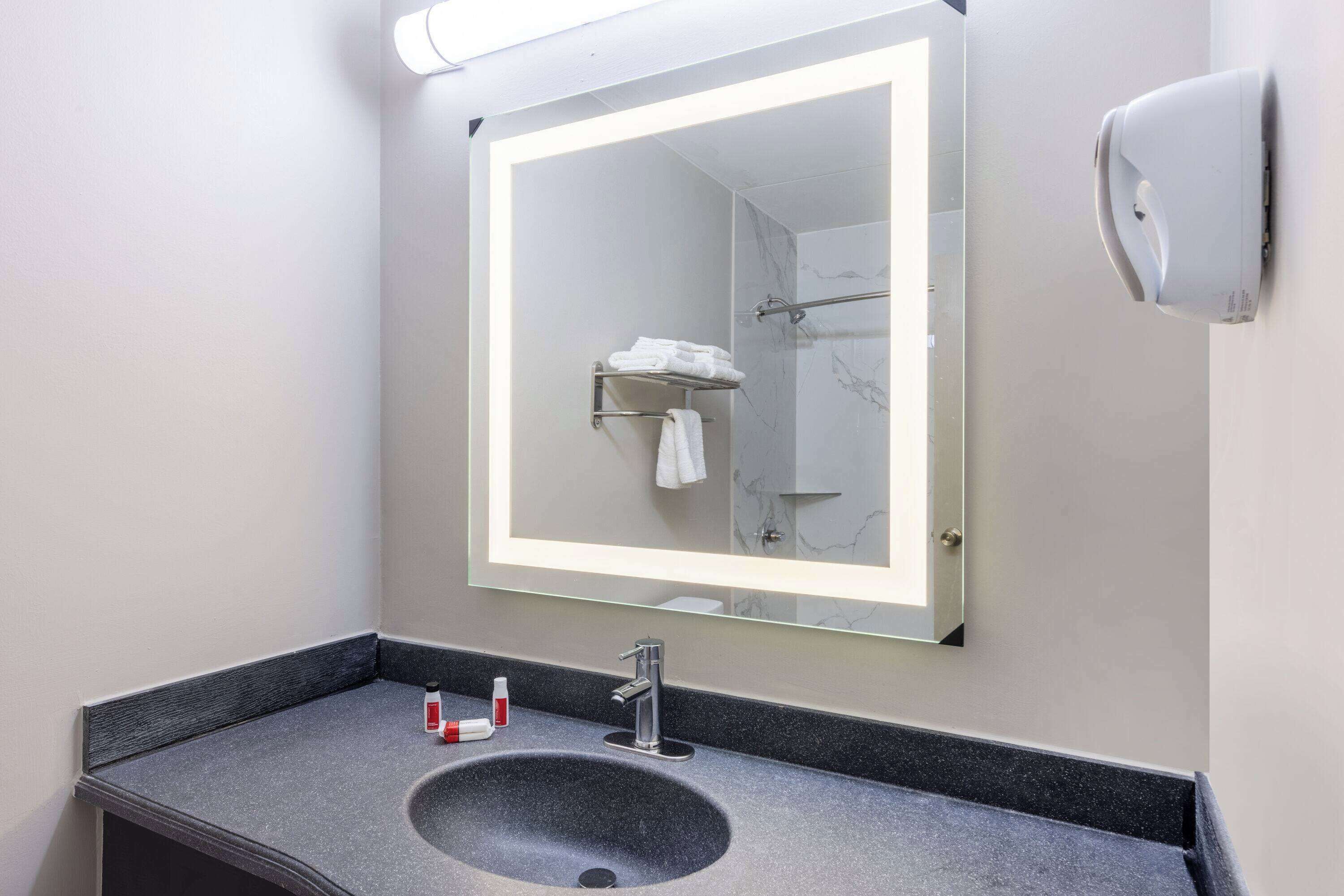 A bathroom with a large mirror, a sink, and a towel rack.